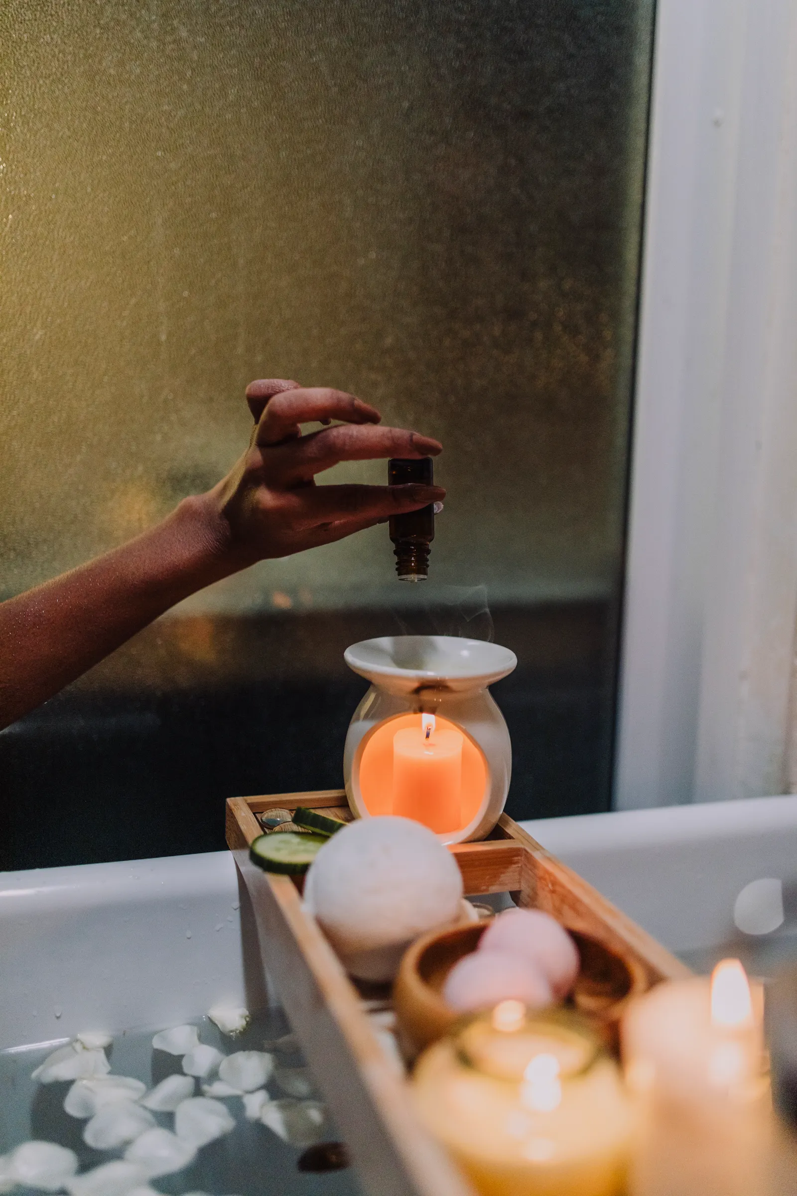 Aromatherapy oil being added to a candle burner beside a lit candle
